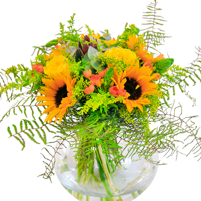The first impression this arrangement gives is an outpouring of golden optimism, reminiscent of a West Ham morning flooded with sun. Majestic sunflowers with rich brown hearts and vivid yellow-orange petals rise above the bouquet, every blossom angled as if searching for light over Stratford's rooftops. Harmonized perfectly, spiraling yellow garden roses add a refined touch, their soft fragrance conjuring memories of community gardens in bloom. Among the sea of bright hues, deep red Hypericum berries create bursts of color, their glossy texture standing in playful contrast to the velvety, matte petals. The greenery is abundant-lush fern fronds, sprays of delicate solidago, and slender, springy spikes imbue the arrangement with energy and life. Artistic touches of eucalyptus introduce a calming blue-green hue, softening the effect and filling the air with a subtle, refreshing scent. The vase's round, transparent design puts the architecture of the stems on full display, a testament to the freshness of each hand-picked element. When sunlight dances across the surface, shadows and highlights intermingle, casting a welcoming, cheerful glow on any West Ham table. This bouquet is a beautiful gesture for celebrations-be it a birthday, reunion, or housewarming-where happiness and connection are at the forefront.