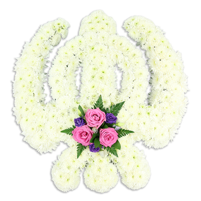 A solemn Sikh Khanda floral tribute is displayed against a spotless white background, every part of the revered symbol fashioned from compact, snowy white chrysanthemums. The blooms are massed so closely that they form a continuous, cushion-like surface, with no stems or gaps visible, allowing the bold shape of the central sword, encircling Chakra, and crossed kirpans to emerge clearly. The tight petals create a fine, almost feathery texture, and the gentle interplay of light and shadow across the surface subtly outlines each component of the emblem. This delicate shading gives the tribute depth and presence, as though the Khanda has been sculpted in fresh petals. At the base of the design, where the curved blades cross, a small but striking bouquet of accent flowers adds colour and emotion. Three pink roses, their petals lush and softly curled, sit among clusters of deep purple blooms and sprays of dark green fern, the foliage and jewel tones creating a sense of grounded, earthly love beneath the serenity of the white. A faint shadow beneath the tribute anchors it to the surface, enhancing the three-dimensional feel. The overall impression is of reverence, purity, and steadfast faith. In West Ham, a piece like this would often be carried into a gurdwara or chapel for a funeral, memorial, or commemorative service, chosen by families who want a floral tribute that honours Sikh tradition while speaking gently of their personal grief and enduring affection.